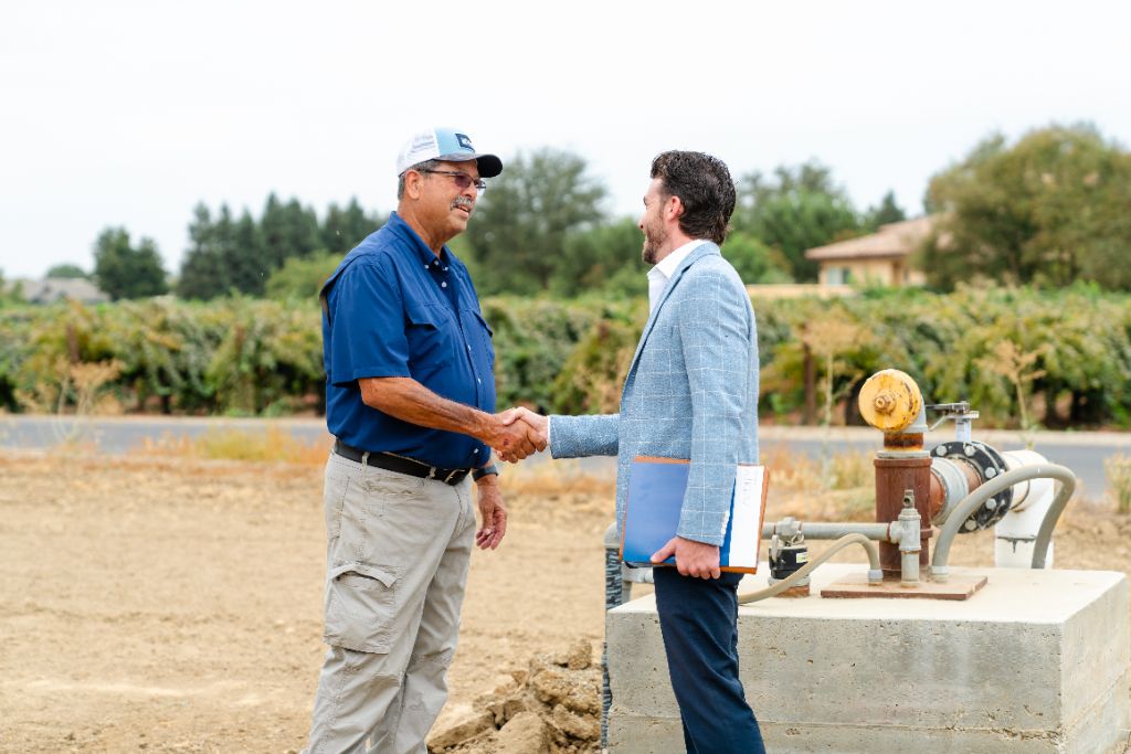 Two people shaking hands at the edge of a Central Valley field